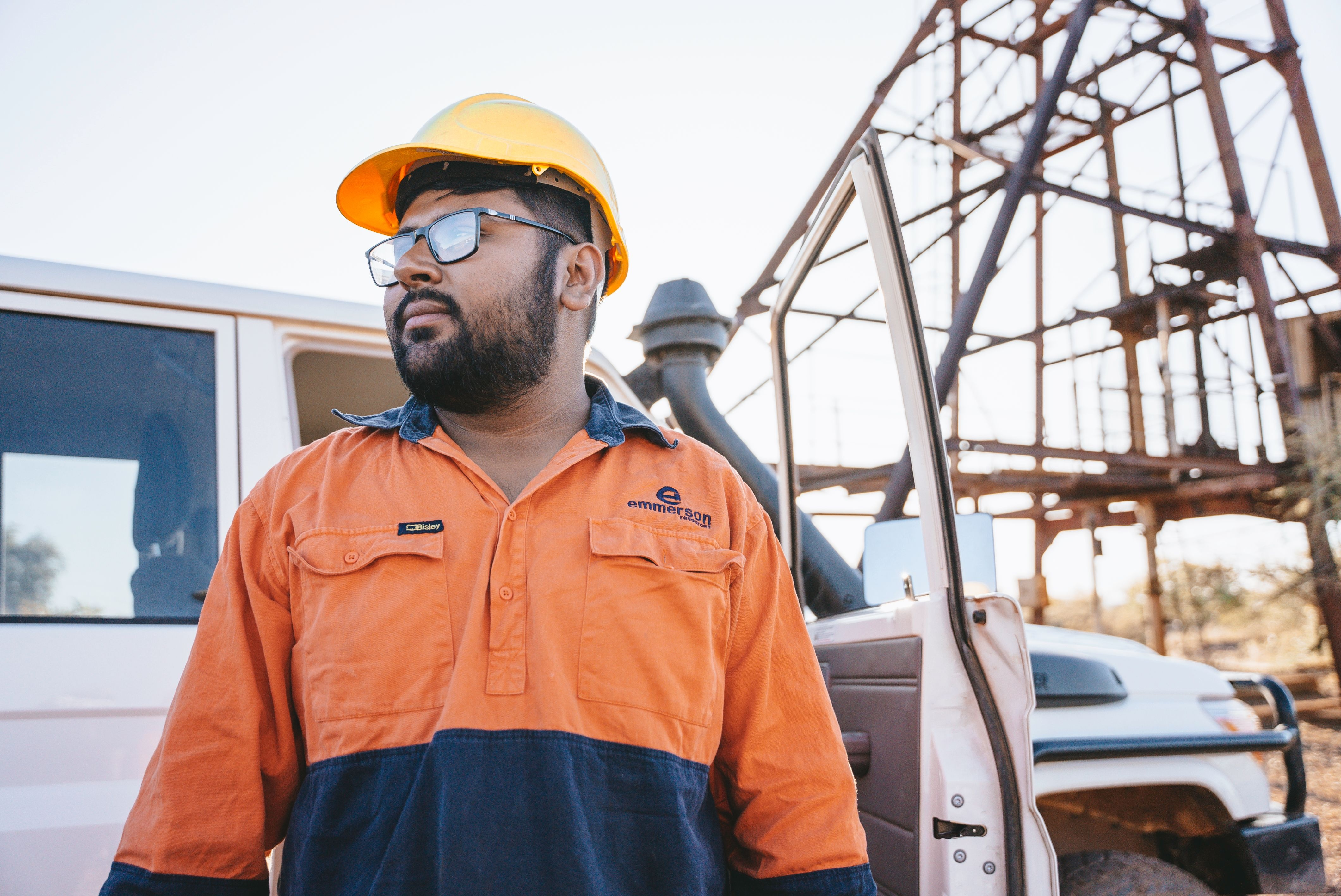 Worker in high-visibility safety clothing and hard hat standing beside a utility vehicle at an industrial worksite.