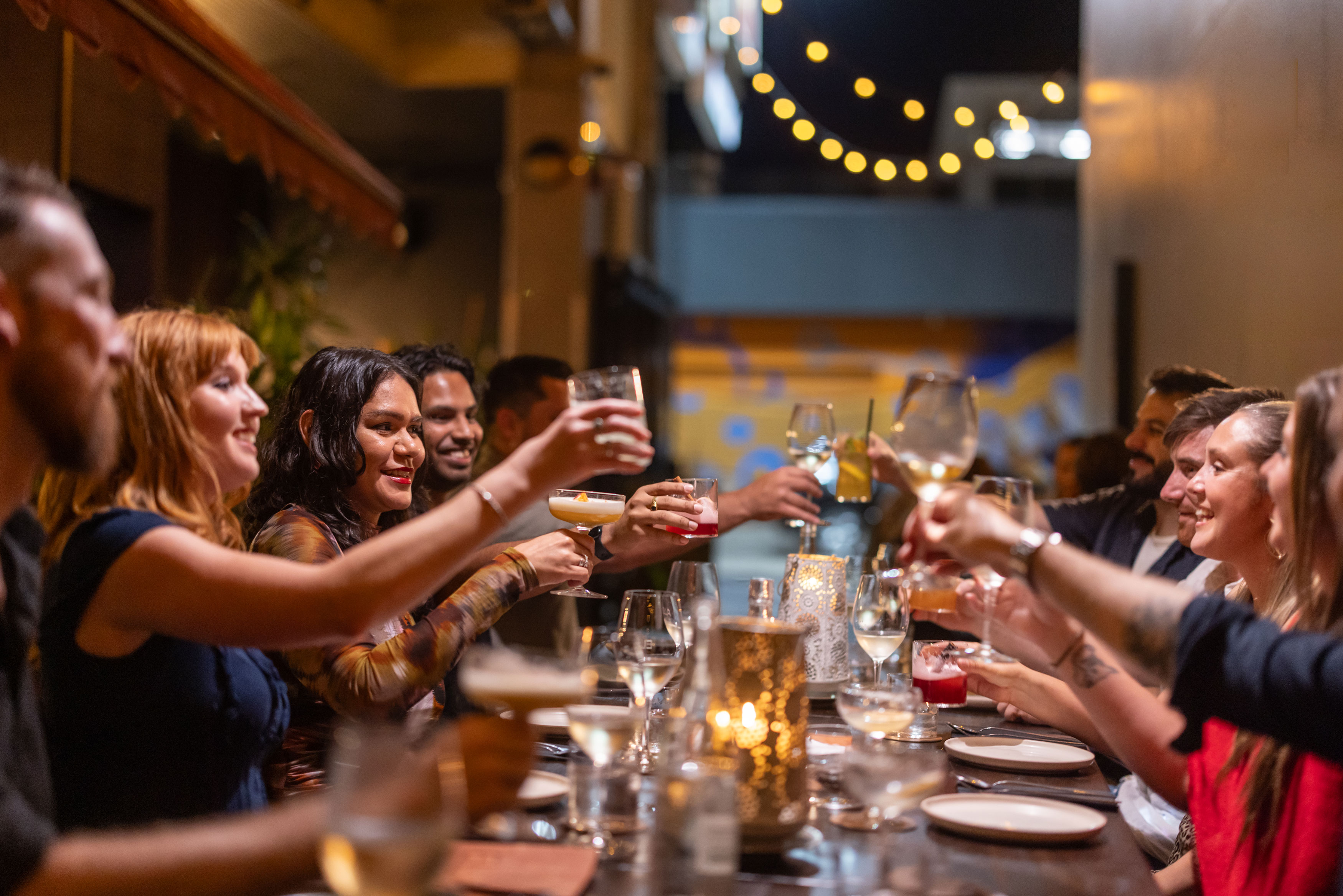 People seated around a long dining table raising glasses during a social gathering.