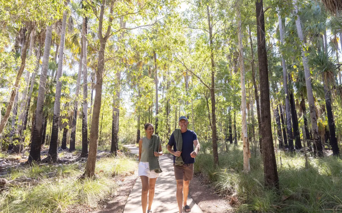 Two people walking through tropical woodland at Bitter Springs