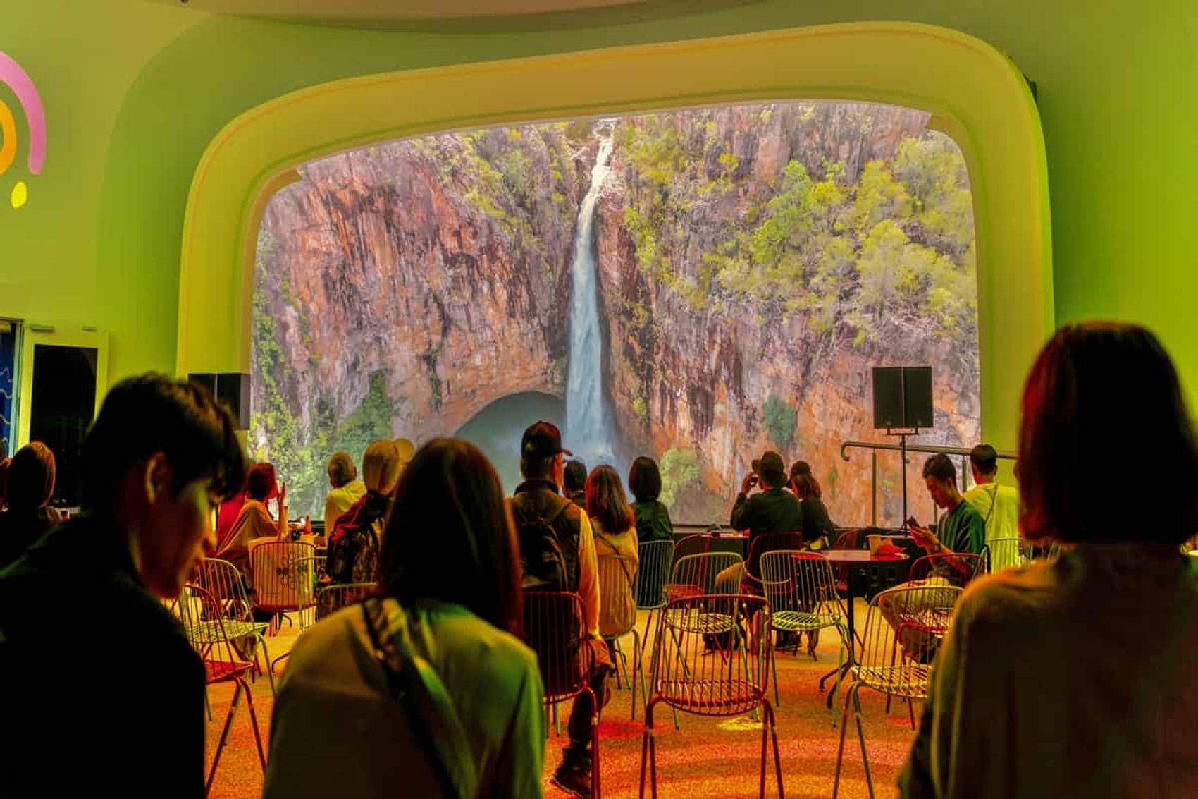 People in a room viewing a large screen displaying a waterfall scene.