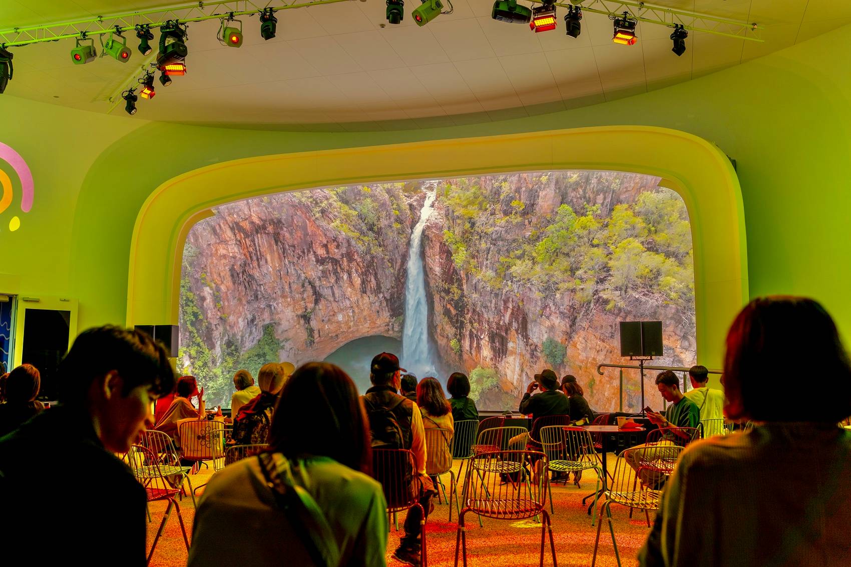 People sitting in a colorful indoor space with a large waterfall view.