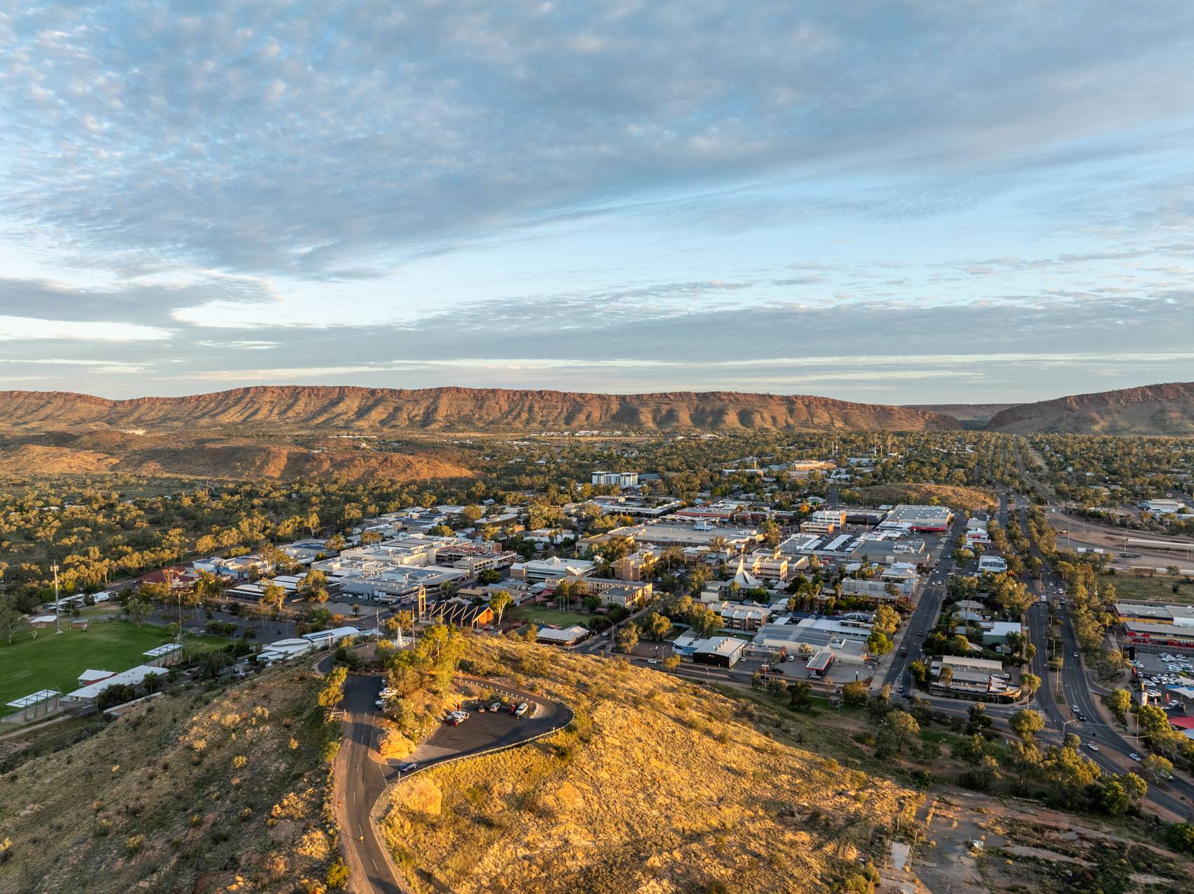 Aerial view of a small city surrounded by arid hills and a vibrant sky.