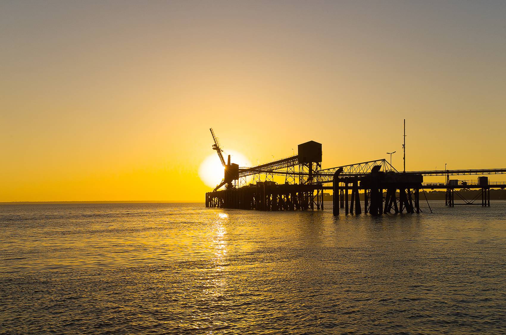 Sunset over an industrial pier silhouetted against a calm ocean.