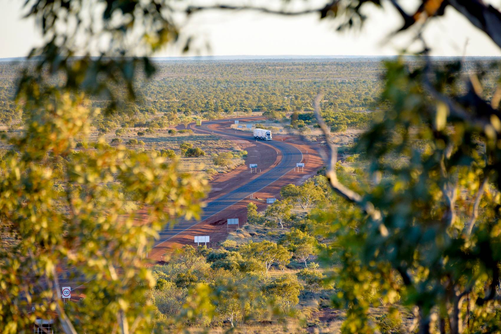 Curving road through vast, open landscape with truck, framed by tree branches.
