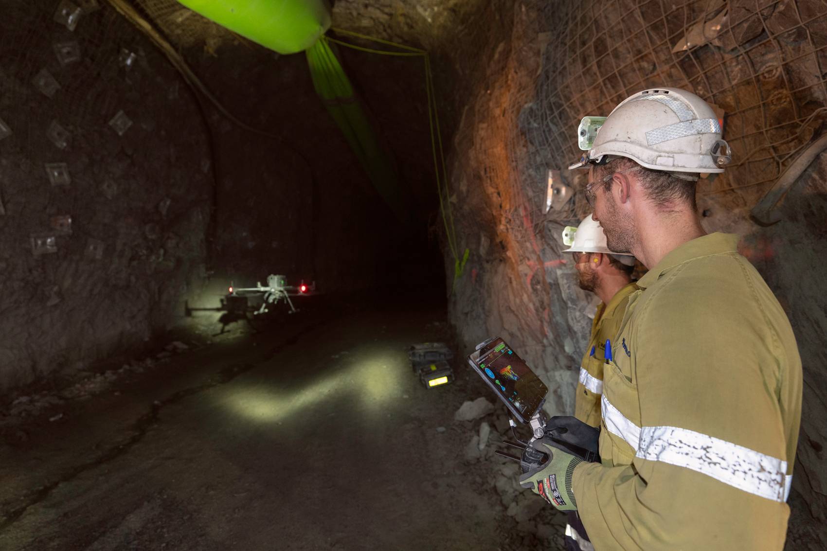Workers operating a drone inside a dimly-lit underground tunnel.