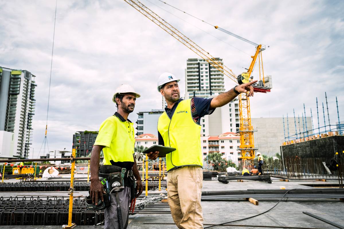 Two construction workers discussing a project with cranes and buildings in the background.
