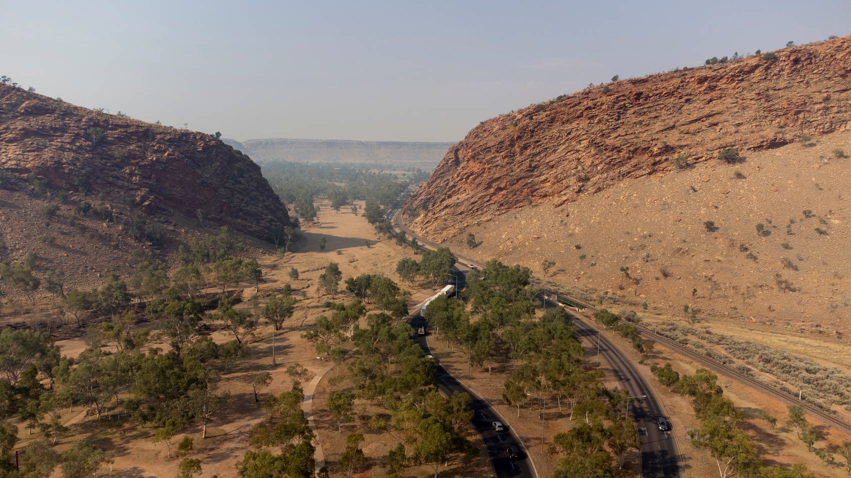 Road winding through a rocky valley flanked by hills and trees.