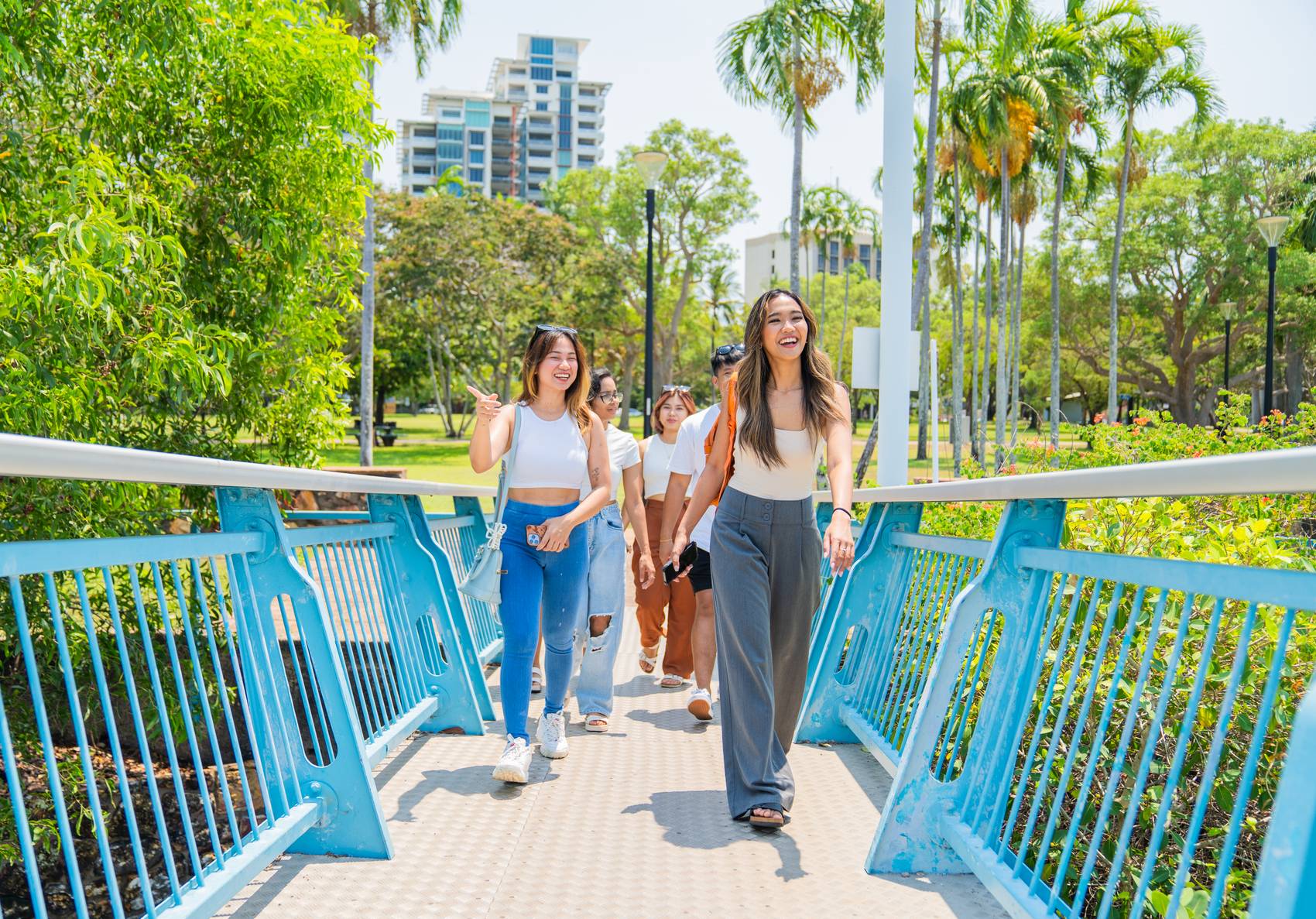 A group of friends walking on a bridge in a sunny park.