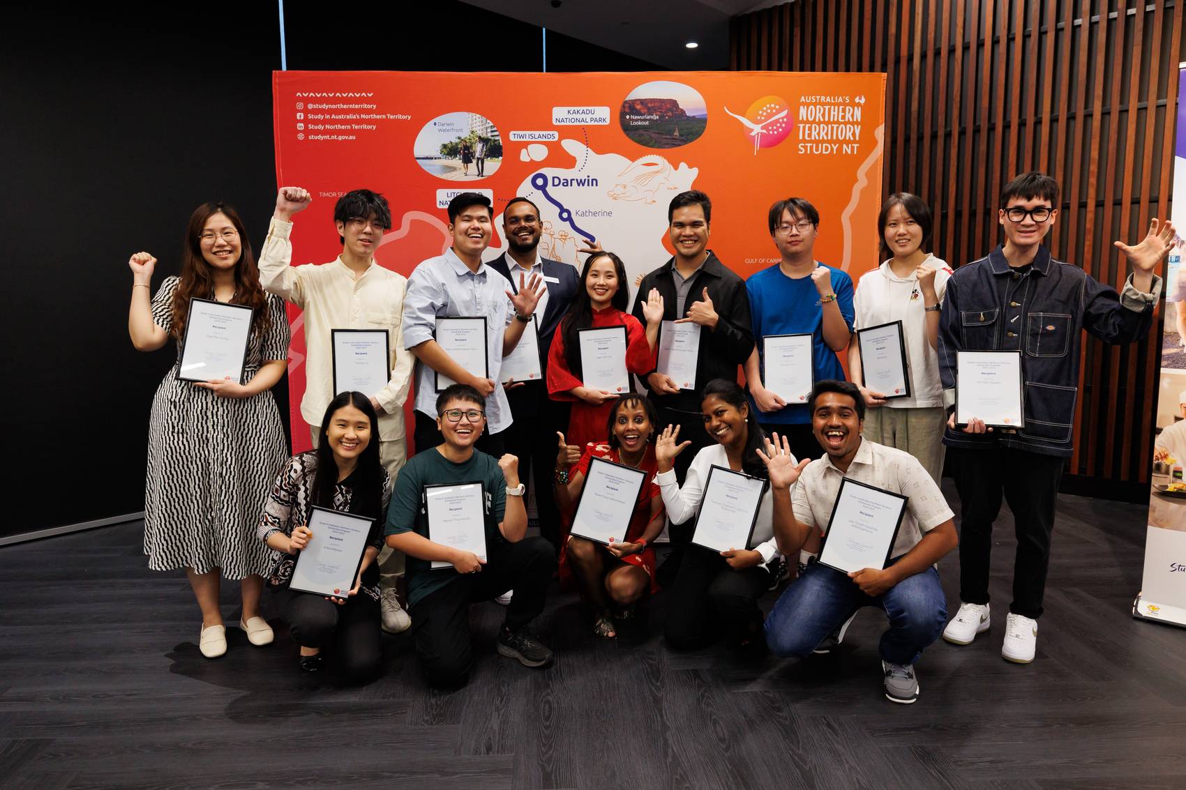 A group of people proudly holding certificates in front of a colorful backdrop.