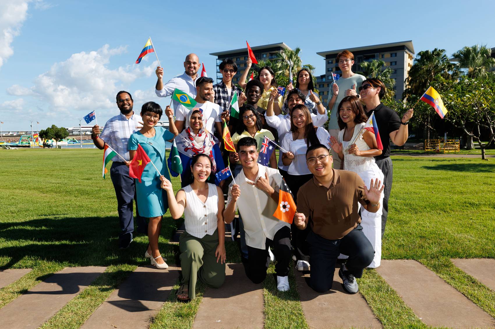 A diverse group of people holding various national flags, smiling outdoors.