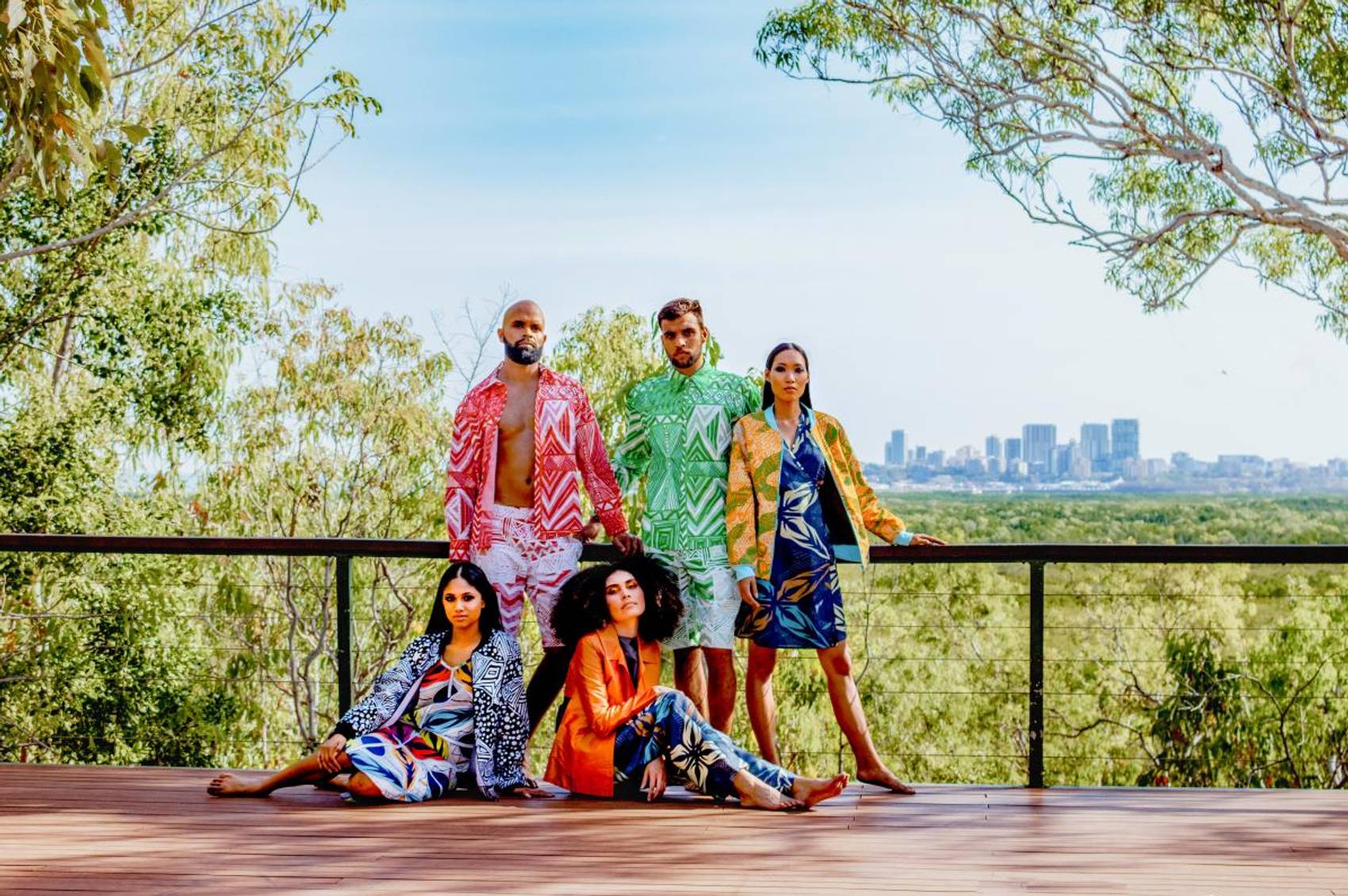 Five people in vibrant outfits on a deck with city view.