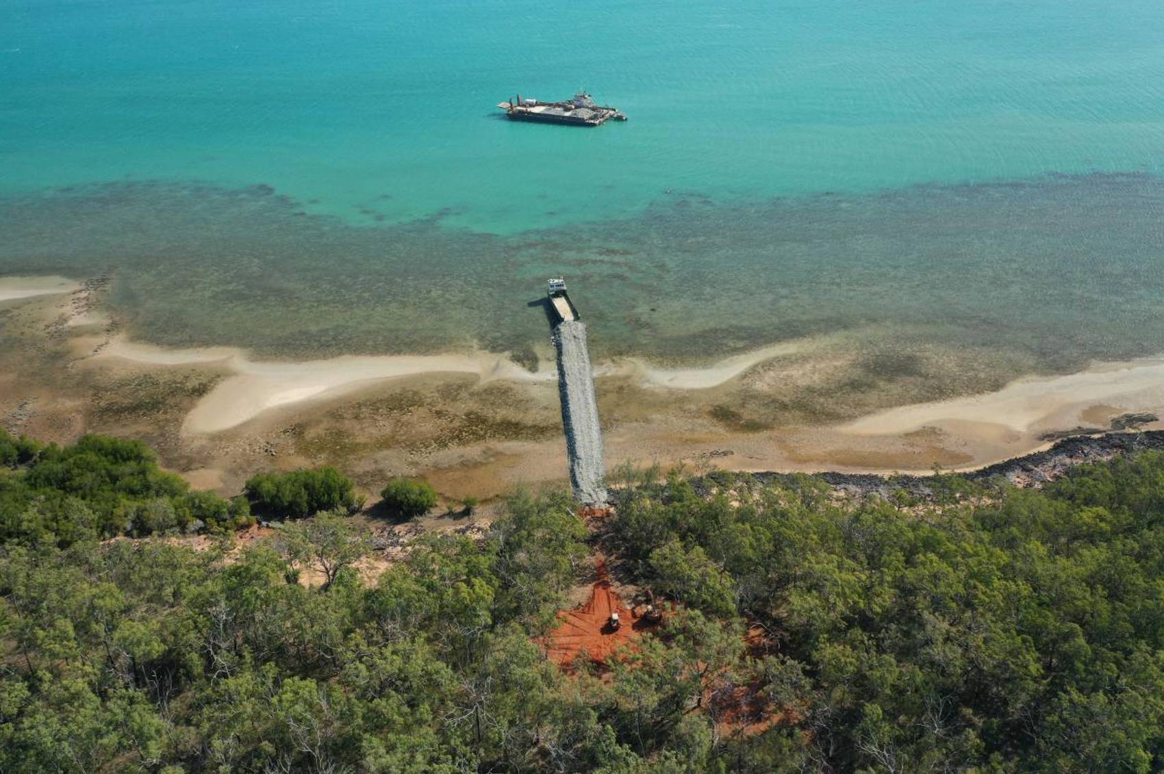 Aerial view of a pier extending into turquoise waters, surrounded by trees.