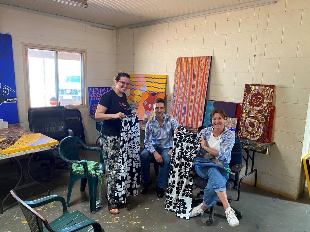 Three people with painted canvases and patterned fabrics in art studio.